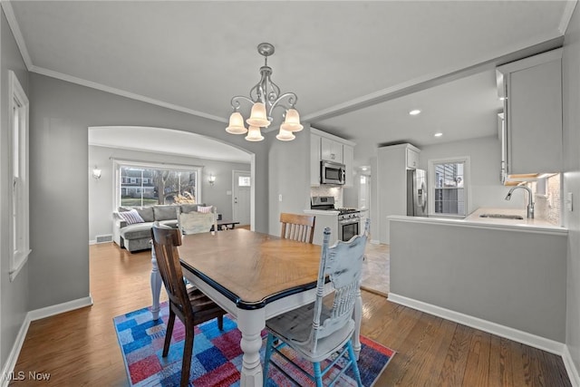 dining space with wood finished floors, arched walkways, a wealth of natural light, and baseboards