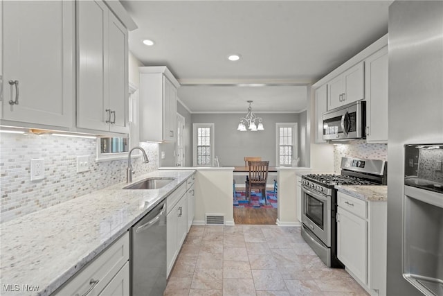 kitchen featuring crown molding, light stone counters, appliances with stainless steel finishes, white cabinetry, and a sink