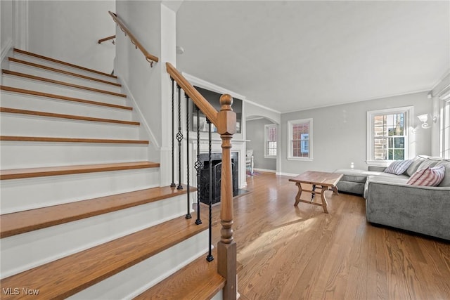 staircase with ornamental molding, wood finished floors, arched walkways, a fireplace, and baseboards