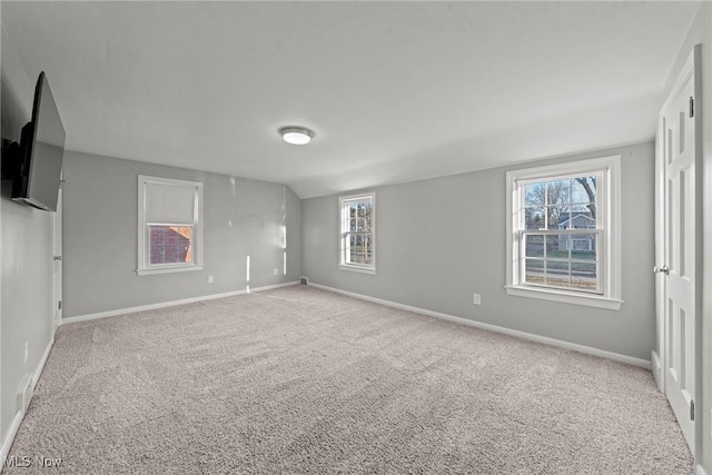 carpeted spare room featuring lofted ceiling and baseboards