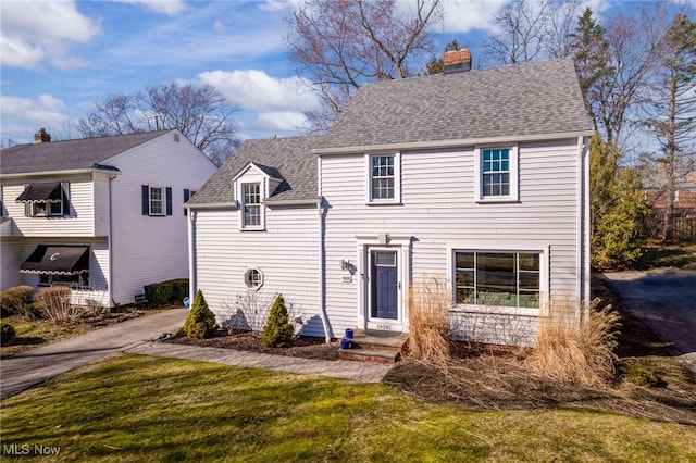 view of front of home with driveway, a front yard, a chimney, and a shingled roof