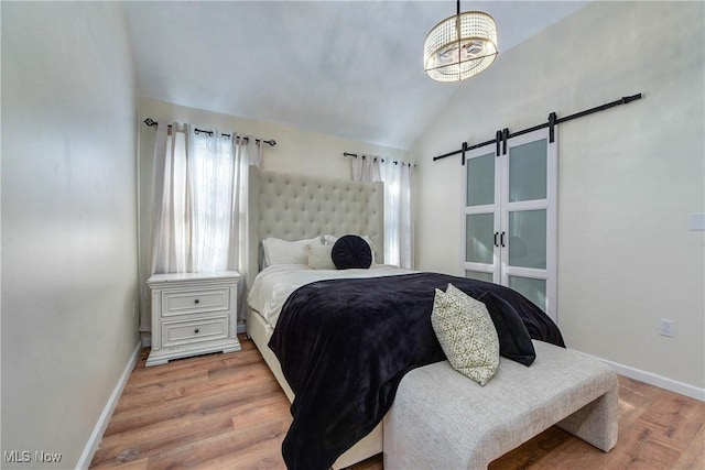 bedroom with a barn door, baseboards, light wood finished floors, and vaulted ceiling