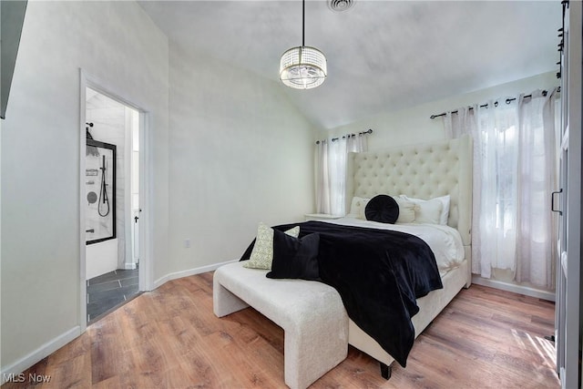 bedroom with baseboards, ensuite bath, lofted ceiling, and wood finished floors