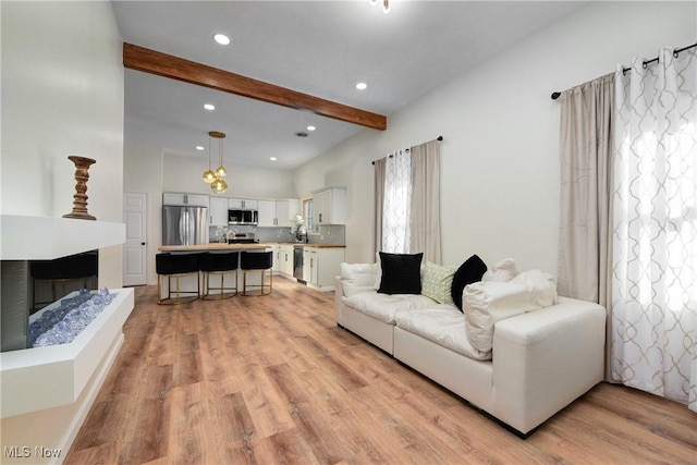 living room featuring recessed lighting, light wood-type flooring, beam ceiling, and a fireplace with raised hearth