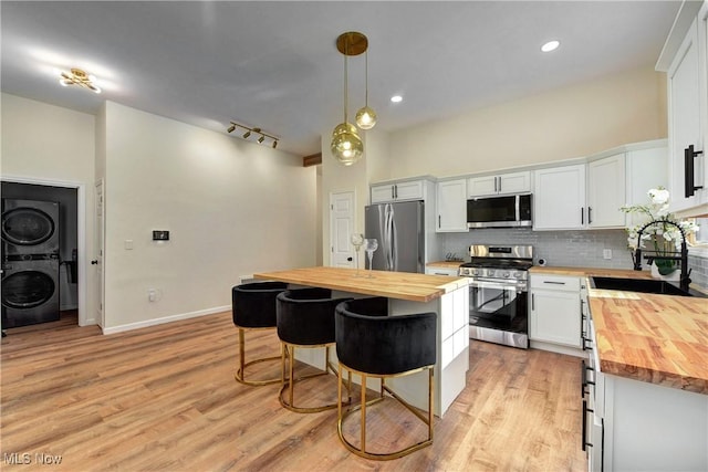 kitchen with stacked washer and dryer, a sink, appliances with stainless steel finishes, butcher block counters, and decorative backsplash