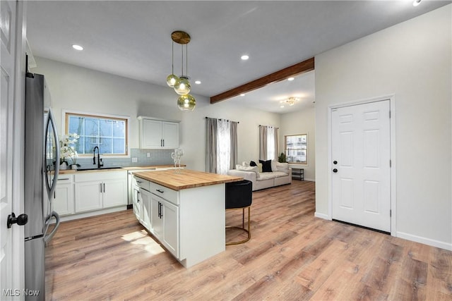 kitchen with a breakfast bar area, freestanding refrigerator, wood counters, white cabinetry, and open floor plan