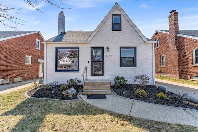 view of front of home with brick siding, a chimney, and a front yard