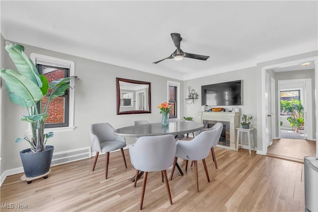 dining space with a ceiling fan, light wood-style flooring, a fireplace, and baseboards