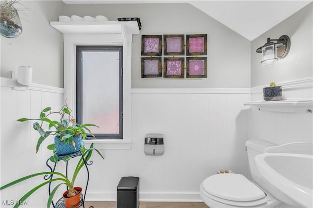 half bathroom featuring a wainscoted wall, lofted ceiling, and toilet