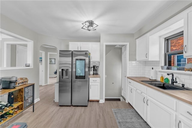 kitchen featuring light wood-style floors, stainless steel refrigerator with ice dispenser, arched walkways, white cabinetry, and a sink