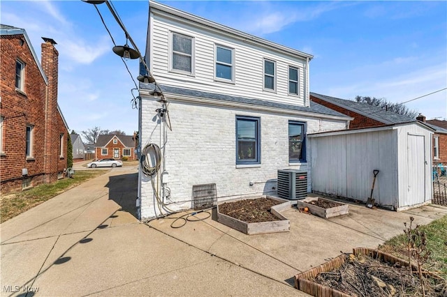 back of property featuring a storage unit, central AC, an outdoor structure, a garden, and brick siding