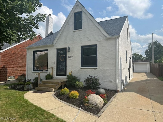 bungalow-style home featuring roof with shingles, a chimney, an outdoor structure, a detached garage, and brick siding