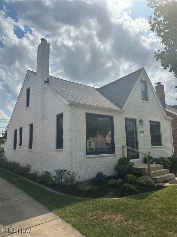 view of front of house featuring brick siding, a chimney, a front lawn, and a shingled roof