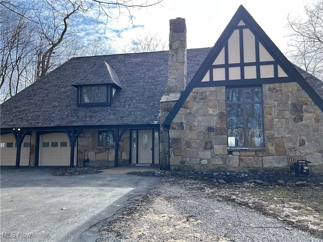 view of front of home featuring aphalt driveway, stone siding, an attached garage, a shingled roof, and a chimney