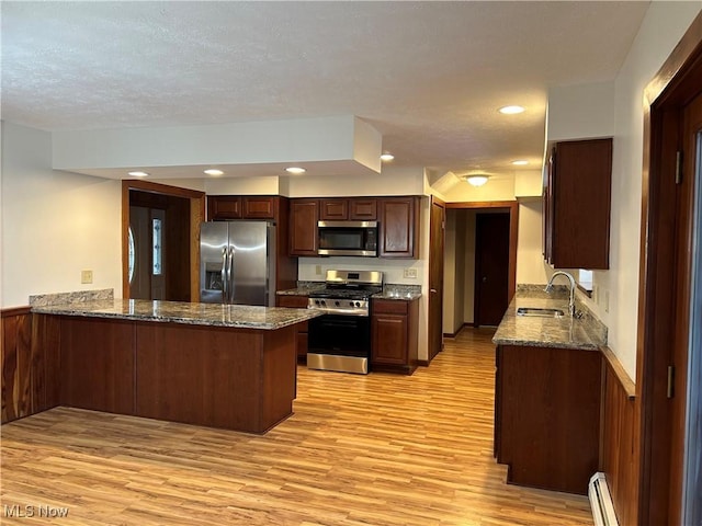 kitchen featuring dark stone counters, appliances with stainless steel finishes, a peninsula, light wood-style floors, and a sink