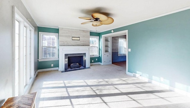 unfurnished living room with a large fireplace, carpet, baseboards, ornamental molding, and a ceiling fan