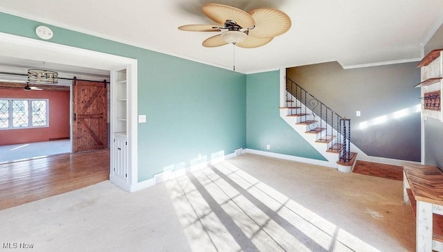 unfurnished living room with a ceiling fan, baseboards, stairs, crown molding, and a barn door