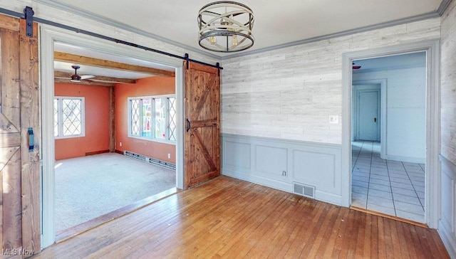 unfurnished room with a barn door, visible vents, hardwood / wood-style floors, and a baseboard radiator