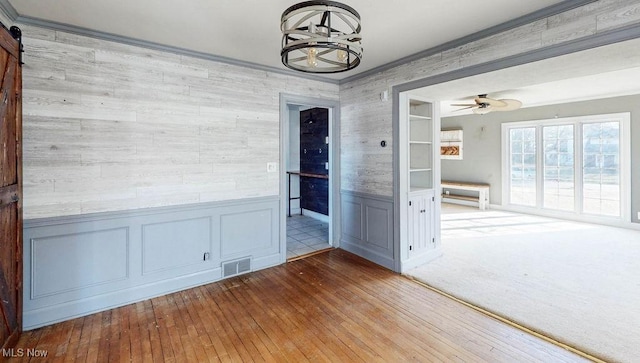 spare room featuring a barn door, ornamental molding, wainscoting, hardwood / wood-style flooring, and a ceiling fan