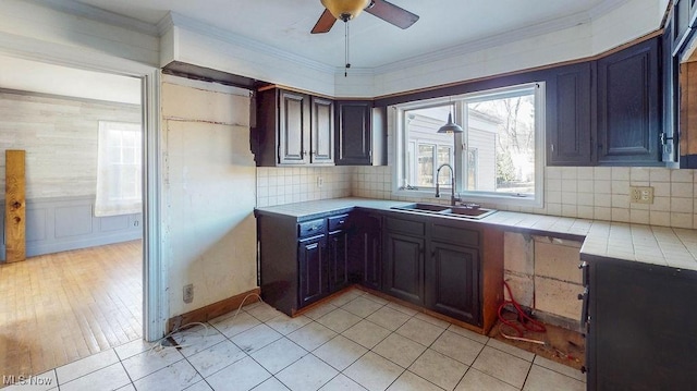 kitchen featuring backsplash, crown molding, tile countertops, light tile patterned floors, and a sink