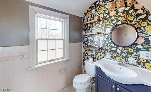 bathroom featuring toilet, tile walls, wainscoting, wallpapered walls, and vanity