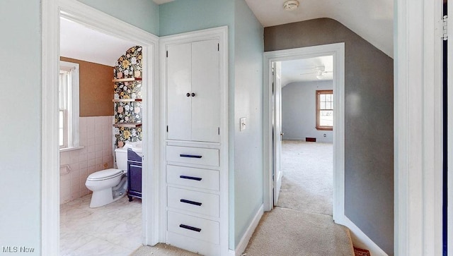 hallway with vaulted ceiling, light colored carpet, tile walls, and baseboards