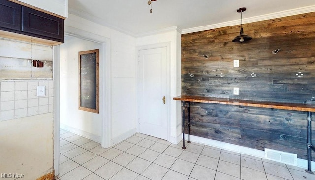 interior space featuring light tile patterned floors, visible vents, wooden walls, and crown molding