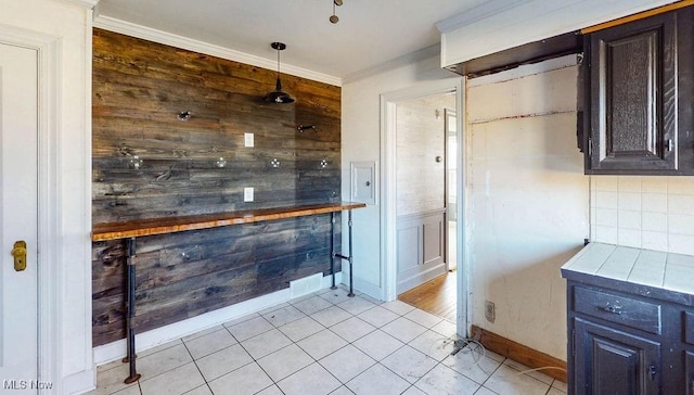 interior space with light tile patterned floors, ornamental molding, decorative backsplash, dark brown cabinetry, and wood walls