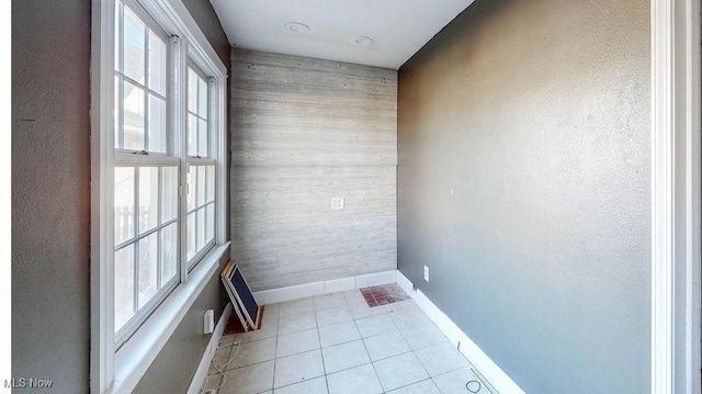 empty room with light tile patterned floors, an accent wall, and baseboards