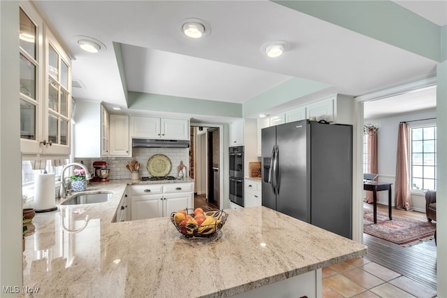 kitchen with stainless steel gas cooktop, a sink, under cabinet range hood, backsplash, and black refrigerator with ice dispenser