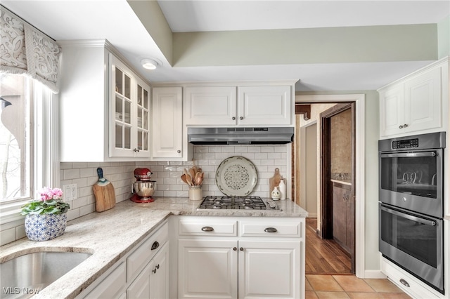 kitchen featuring decorative backsplash, under cabinet range hood, appliances with stainless steel finishes, white cabinets, and glass insert cabinets