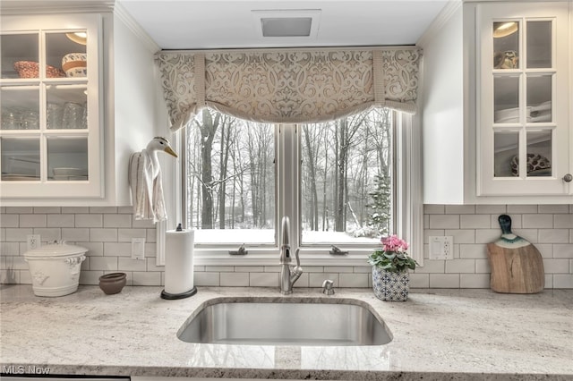 kitchen with white cabinets, light stone countertops, glass insert cabinets, and a sink