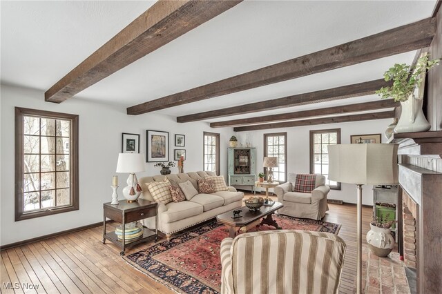 living area with beamed ceiling, light wood-style flooring, a fireplace, and baseboards