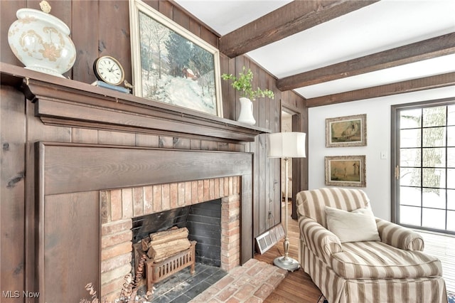 living area featuring beamed ceiling, visible vents, wood finished floors, and a fireplace