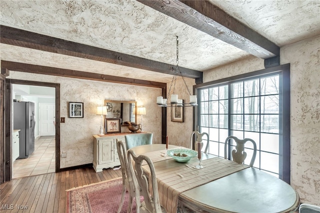 dining space featuring an inviting chandelier, beam ceiling, and light wood finished floors