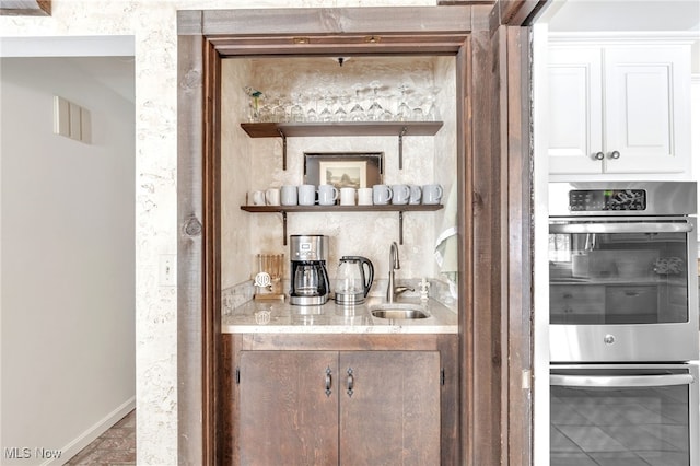 bar featuring indoor wet bar, double oven, baseboards, and a sink