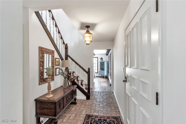 entrance foyer featuring stairway, baseboards, and brick floor