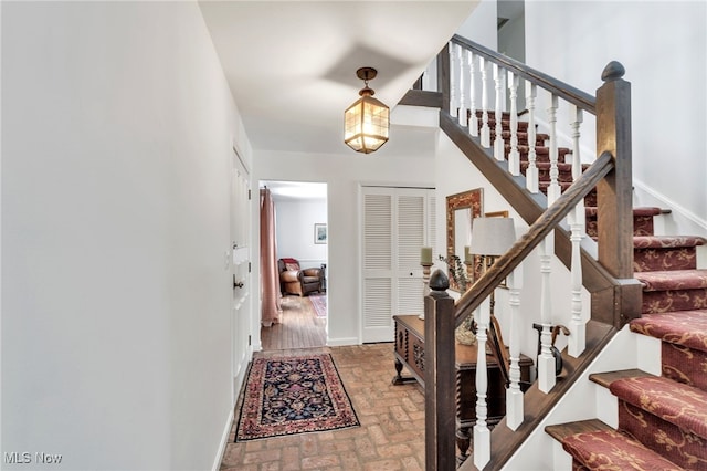 foyer featuring brick floor, baseboards, and stairs