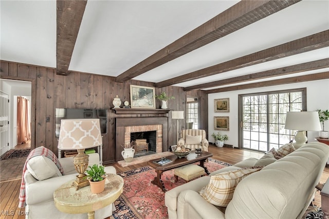 living area featuring beamed ceiling, a healthy amount of sunlight, wood finished floors, and wood walls