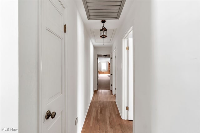 hall with attic access, baseboards, and light wood finished floors