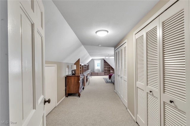 corridor featuring lofted ceiling, carpet flooring, and baseboards