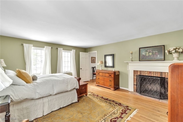 bedroom with baseboards, a brick fireplace, and wood finished floors