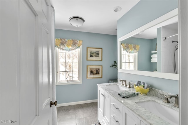 full bathroom featuring double vanity, a shower, baseboards, and a sink