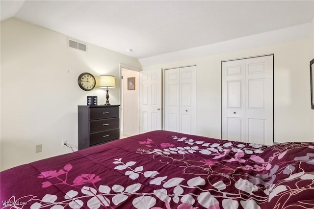 bedroom featuring vaulted ceiling, visible vents, and two closets