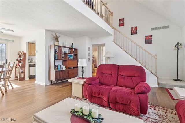 living area with stairway, wood finished floors, visible vents, baseboards, and a towering ceiling