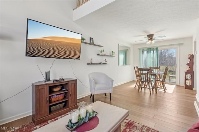 living room featuring a textured ceiling, light wood-style flooring, baseboards, and ceiling fan