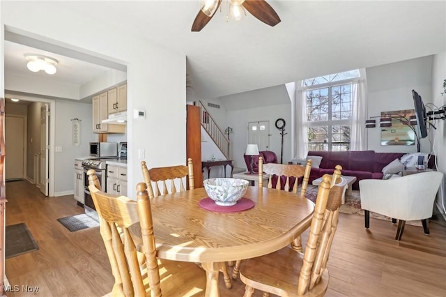 dining area with stairway, baseboards, light wood-type flooring, and ceiling fan