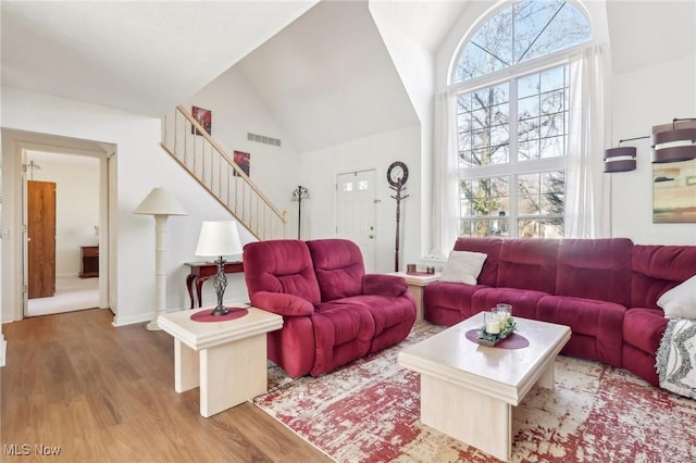 living room with stairs, wood finished floors, visible vents, and high vaulted ceiling