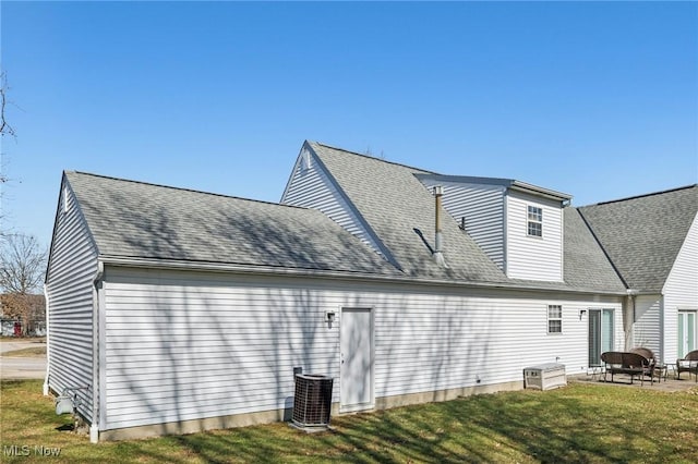 rear view of property featuring cooling unit, a lawn, a patio, and roof with shingles