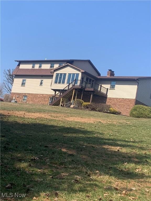 rear view of property featuring a yard, a chimney, a deck, and stairs